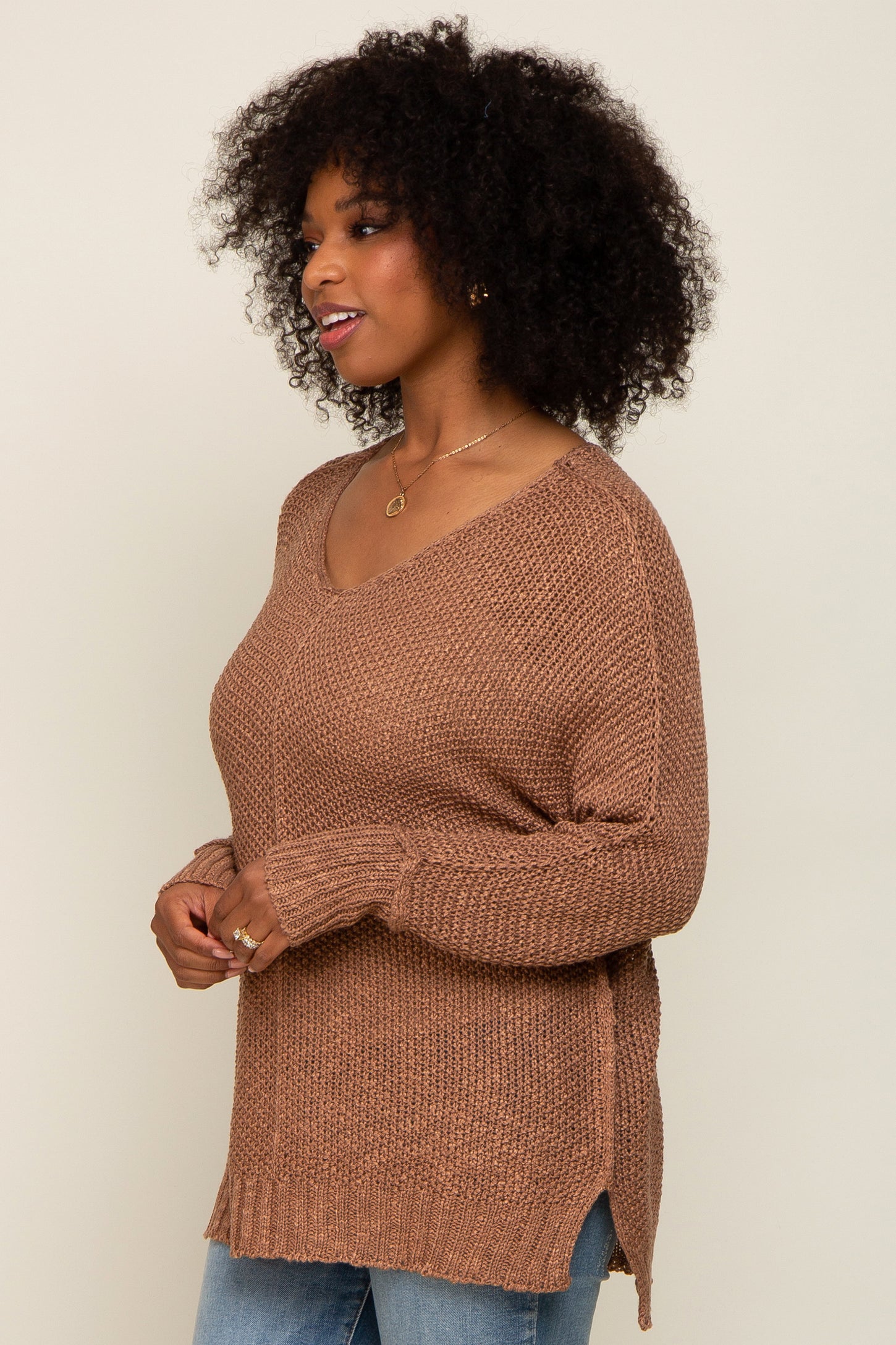 woman wearing a brown oversized v-neck knit sweater with side slits and paired with light blue jeans