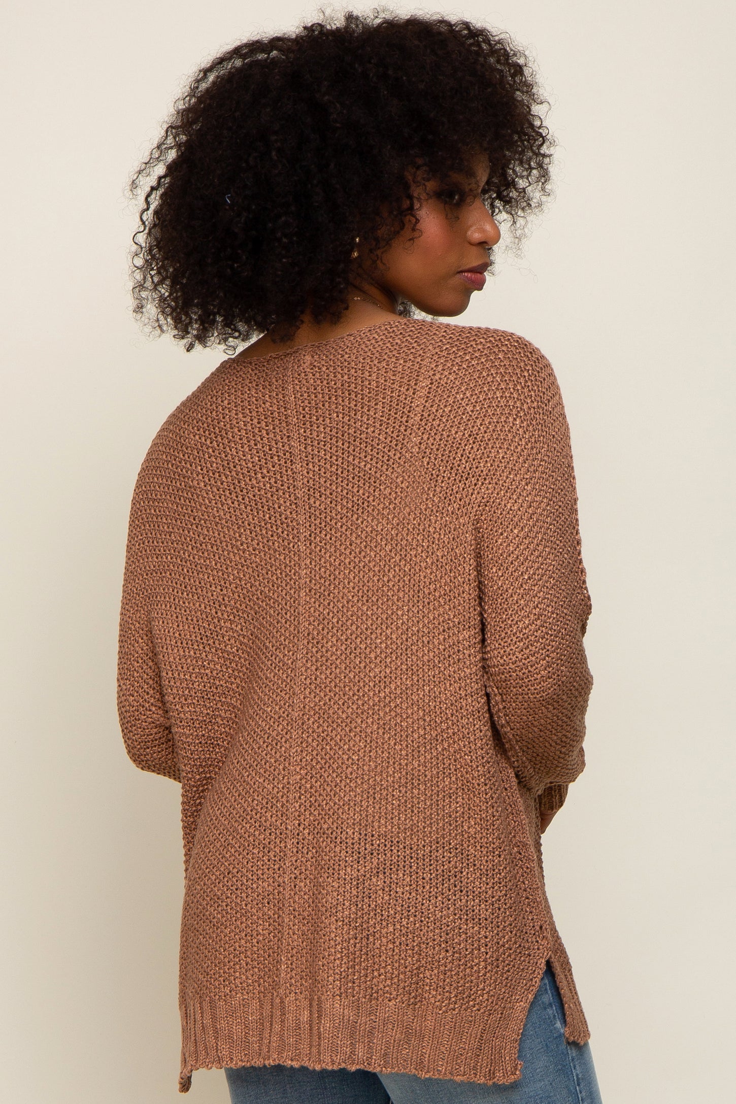 woman wearing a brown oversized knitted sweater with a textured finish and side slits, viewed from the back