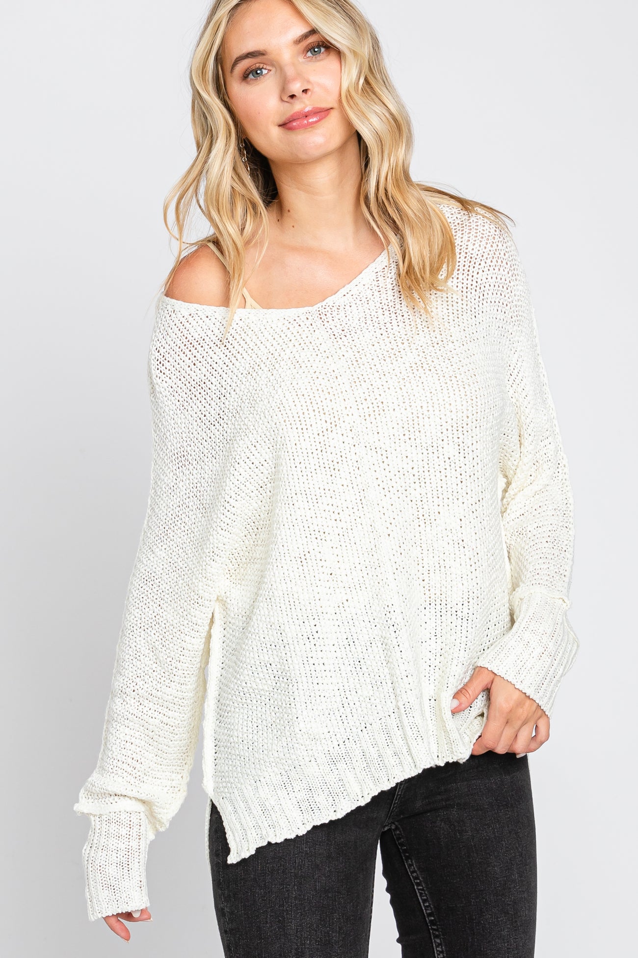 woman wearing an off-white oversized knit sweater with a scooped neckline and side slits, paired with black jeans