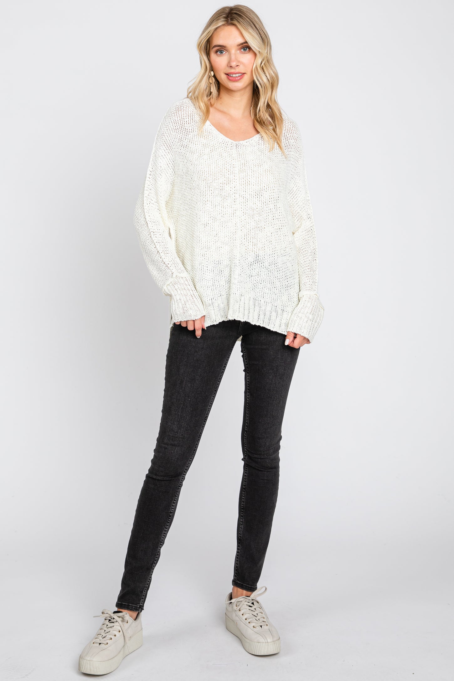 woman wearing a white oversized knit sweater and black skinny jeans, paired with cream-colored sneakers