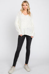 woman wearing a white oversized knit sweater and black skinny jeans, paired with cream-colored sneakers