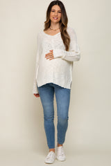 pregnant woman wearing a white knit maternity sweater and blue jeans