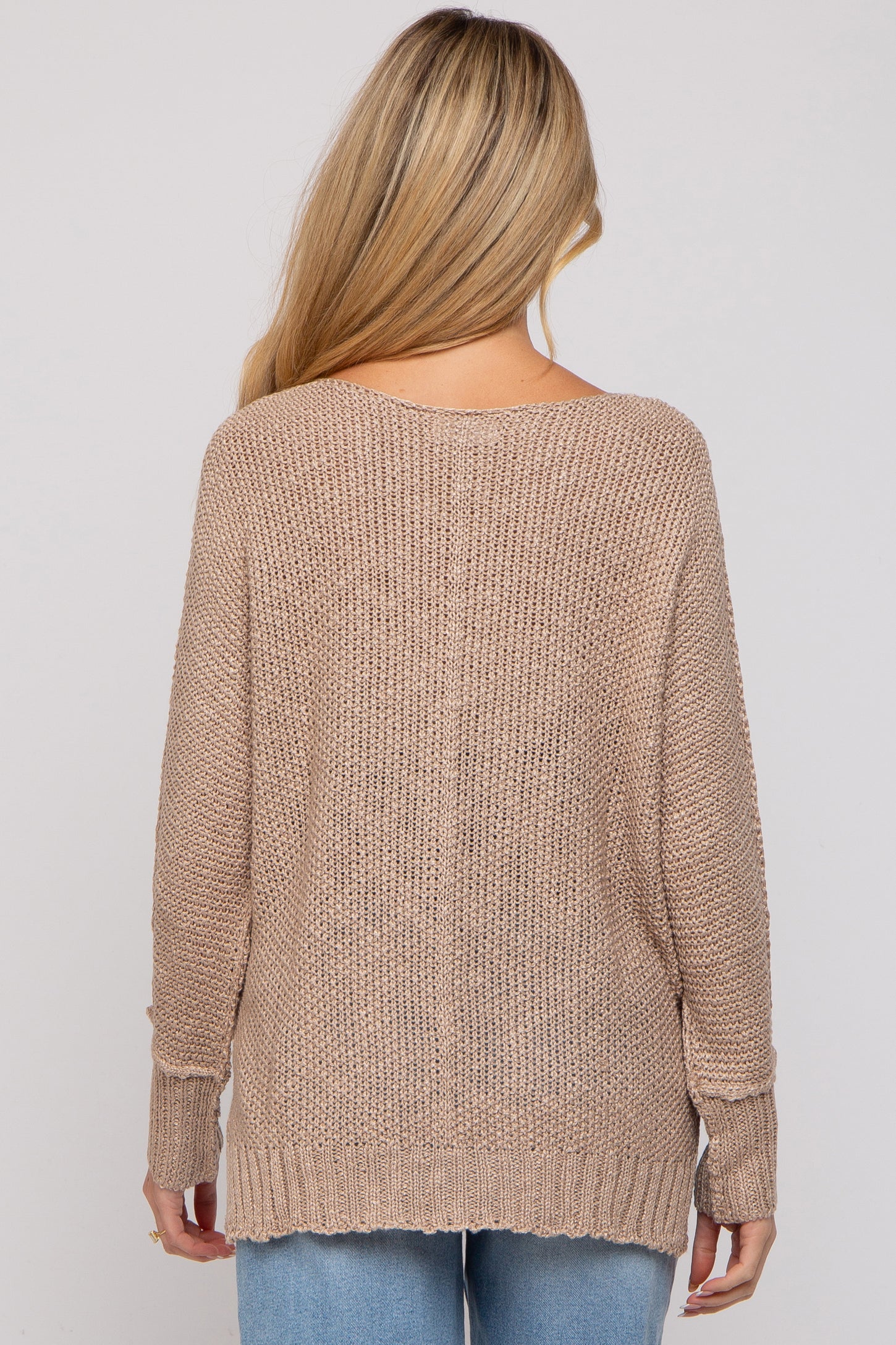 woman wearing a beige loosely knit maternity sweater with long sleeves, viewed from the back