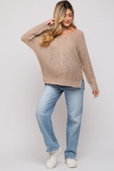 woman wearing a beige oversized maternity sweater and blue distressed jeans, with a baby bump visible