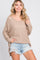 woman wearing a beige loose-knit sweater with a scoop neckline and side slits, paired with distressed denim shorts