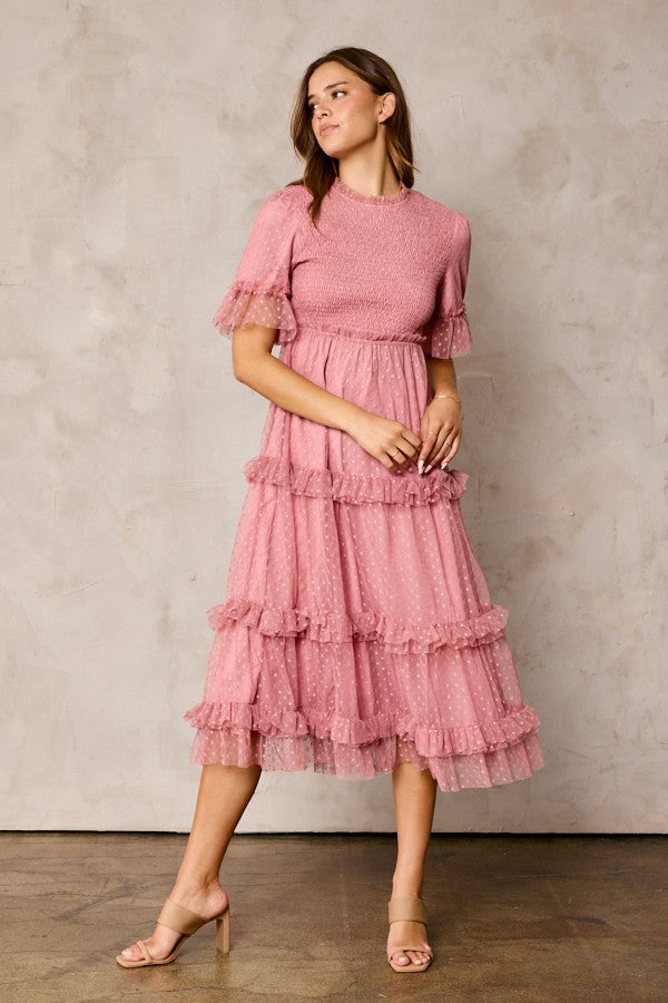 woman wearing a pink midi dress with ruffle details and puff sleeves standing against a neutral background