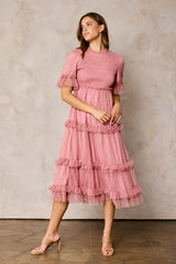 woman wearing a pink midi dress with ruffle details and puff sleeves standing against a neutral background
