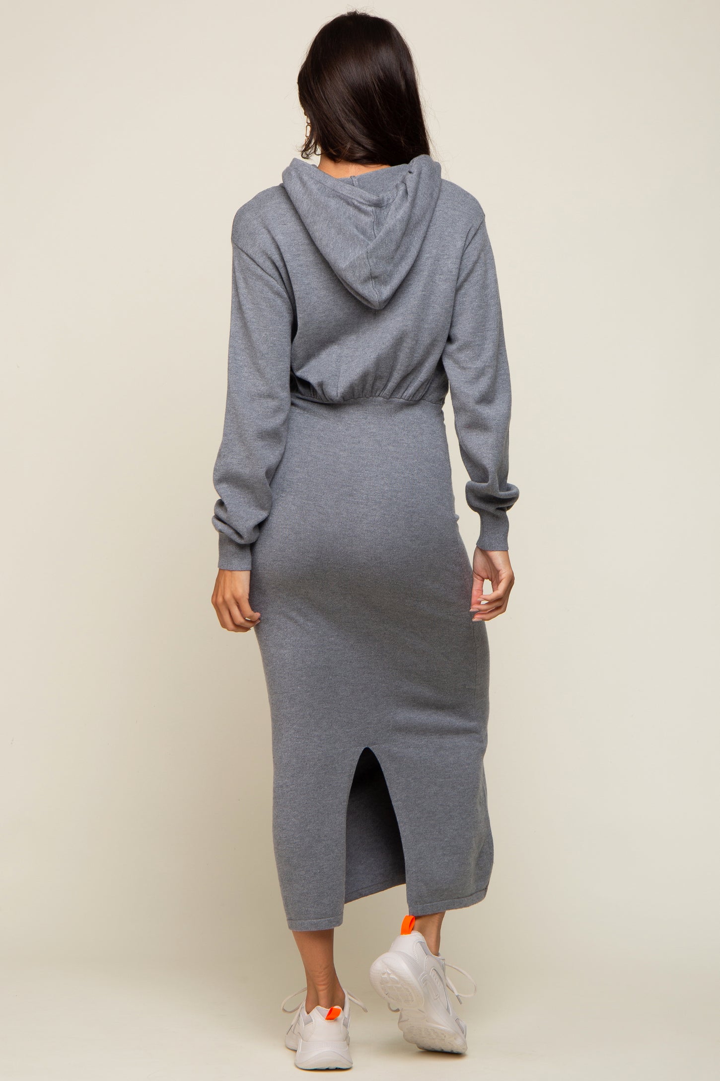 woman wearing a gray hoodie dress with a fitted silhouette and back slit, standing with her back to the camera