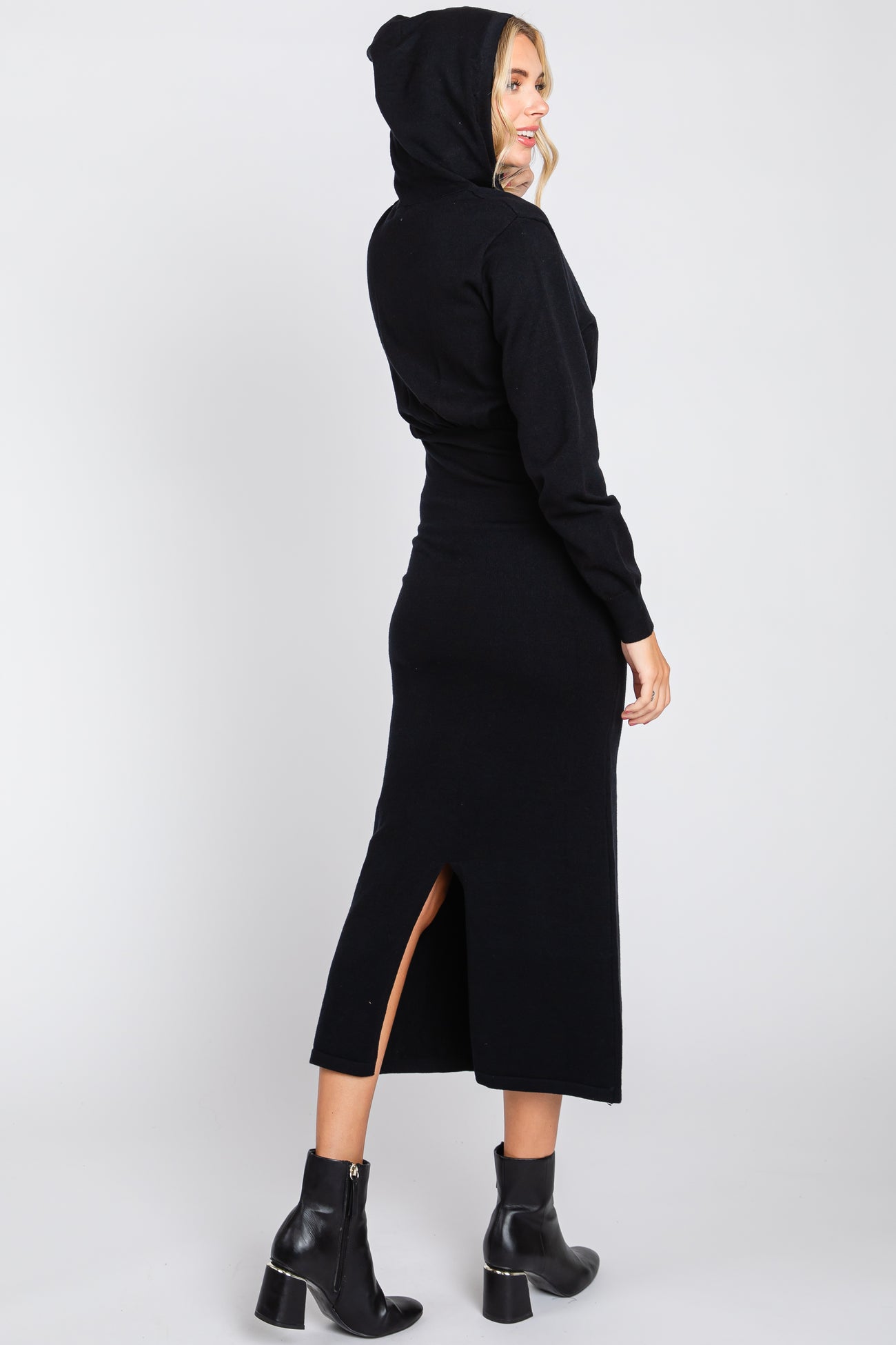 woman wearing a black hoodie dress with a back slit and a fitted silhouette, styled with black ankle boots
