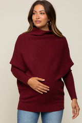 woman wearing a burgundy maternity sweater with a draped neckline and holding her baby bump