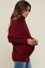 woman wearing a burgundy maternity turtleneck sweater, gently holding her baby bump while smiling