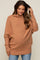 woman wearing a brown oversized maternity sweater with a cowl neck and relaxed fit, showcasing her baby bump