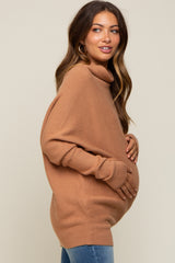 woman wearing a rust colored oversized turtleneck maternity sweater and holding her baby bump