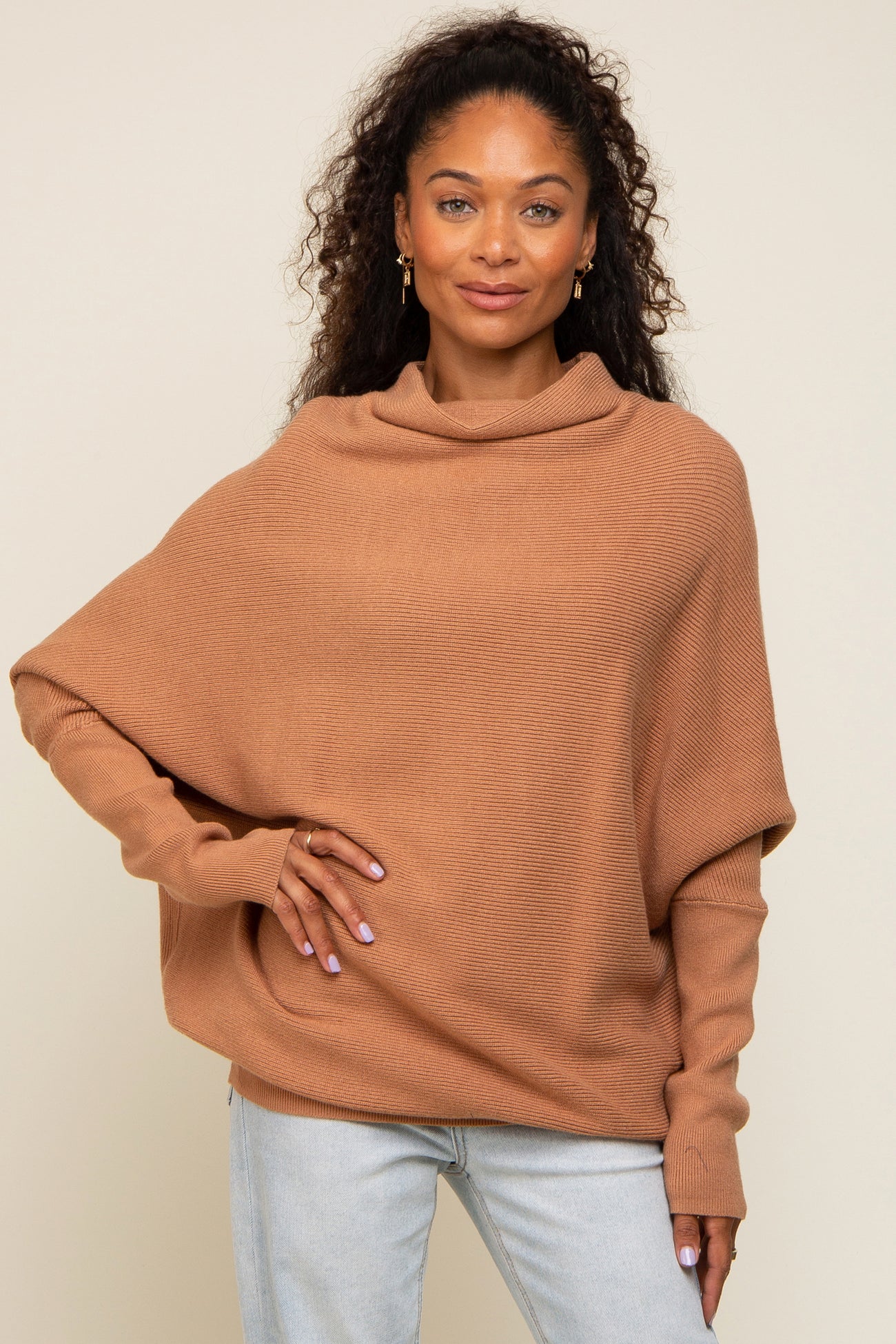 woman wearing a tan oversized knit sweater with a cowl neck and long sleeves, paired with light blue jeans