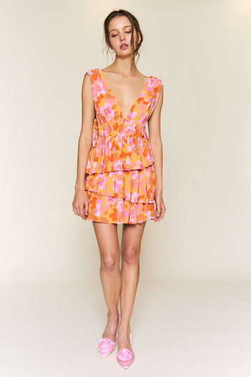 woman wearing a pink and orange floral mini dress with a deep v-neck and tiered ruffles, paired with pink flats