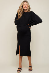 woman wearing a black maternity sweater and matching skirt with a side slit, showing her baby bump