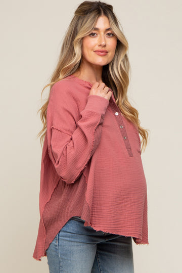 woman wearing a dusty rose maternity top with buttons and raw hem, gently cradling her baby bump