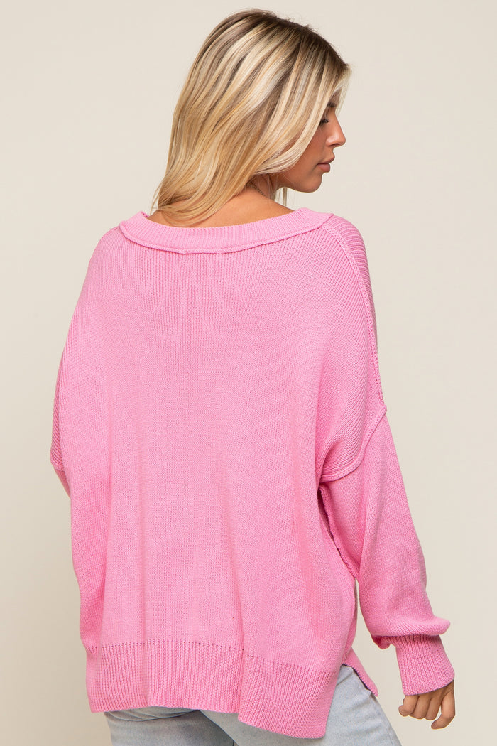 woman wearing a loose-fitting pink oversized sweater with a wide neckline and long sleeves