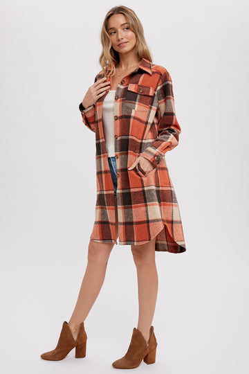 woman wearing an orange and brown plaid shirt dress with long sleeves and pockets, paired with brown heeled ankle boots