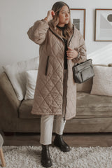 woman wearing a long tan quilted puffer coat, white jeans, and black boots holding a black leather handbag