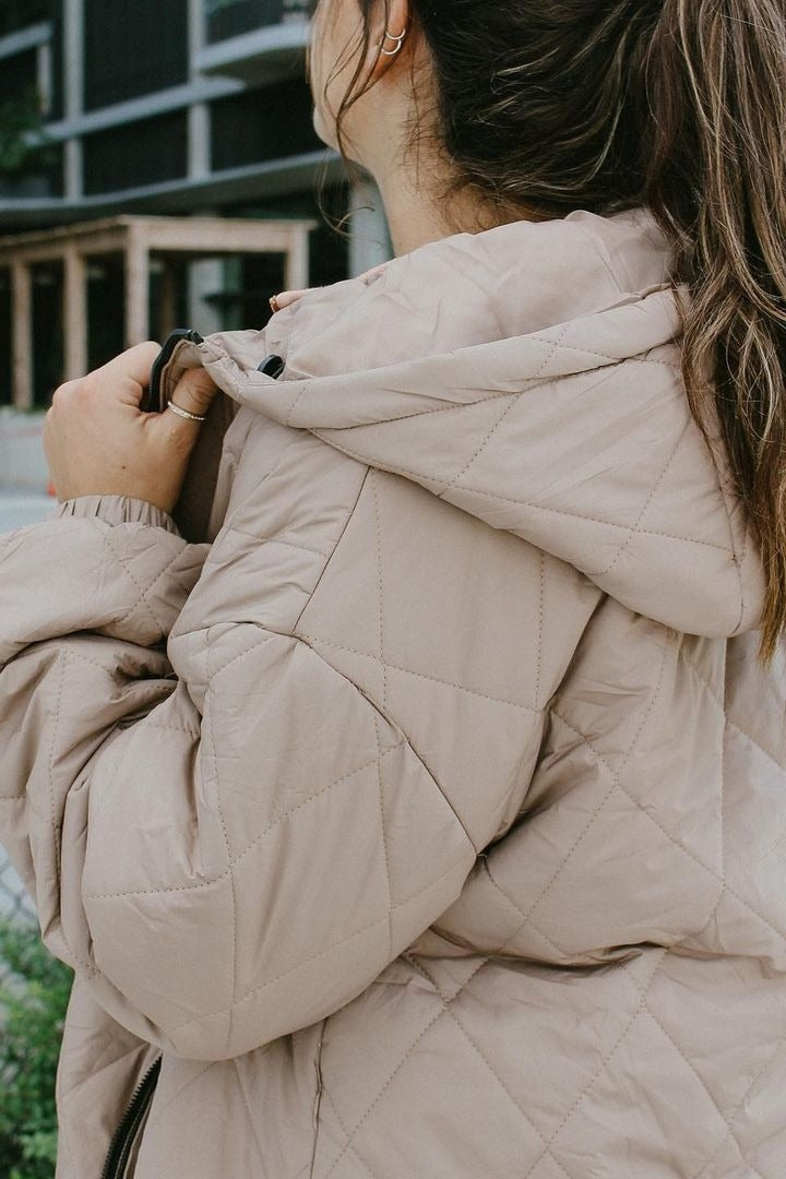 woman wearing a tan quilted puffer jacket with a hood, showing the back and side profile