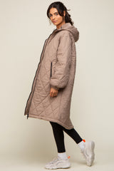 Woman wearing a long taupe quilted puffer coat with a hood, black leggings, and white sneakers
