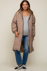 woman wearing a beige quilted maternity coat over a grey top and distressed jeans, showing her baby bump