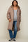 woman wearing a beige quilted maternity coat over a grey top and distressed jeans, showing her baby bump