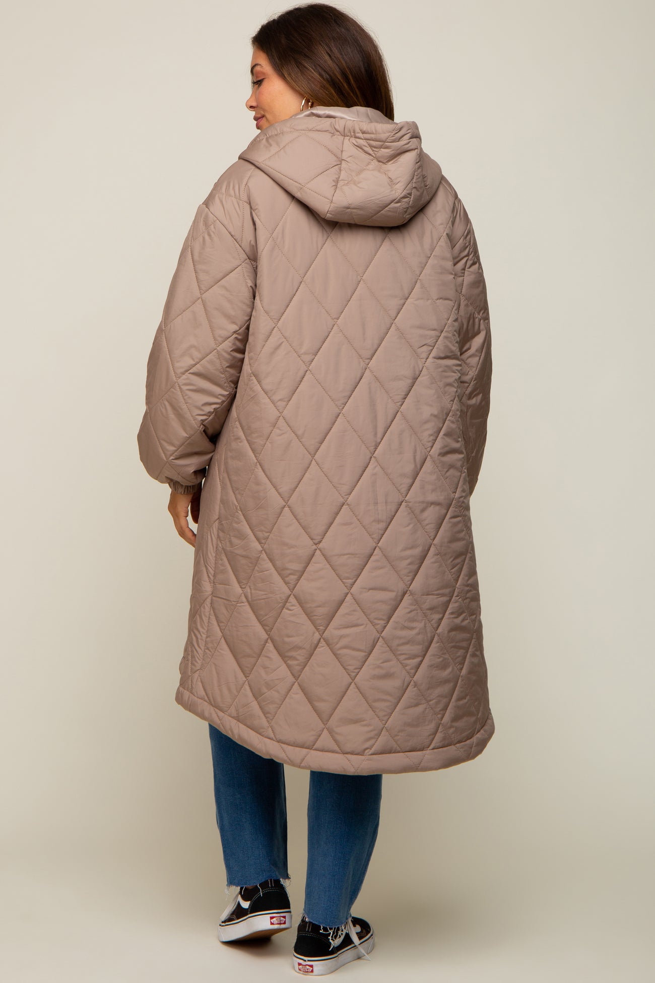 woman wearing a long beige quilted maternity coat with a hood, viewed from the back