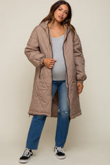 woman wearing a light brown maternity puffer coat over a gray top and blue jeans, showing her baby bump