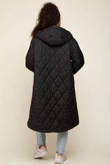 woman wearing a black quilted long coat with a hood, standing with her back to the camera
