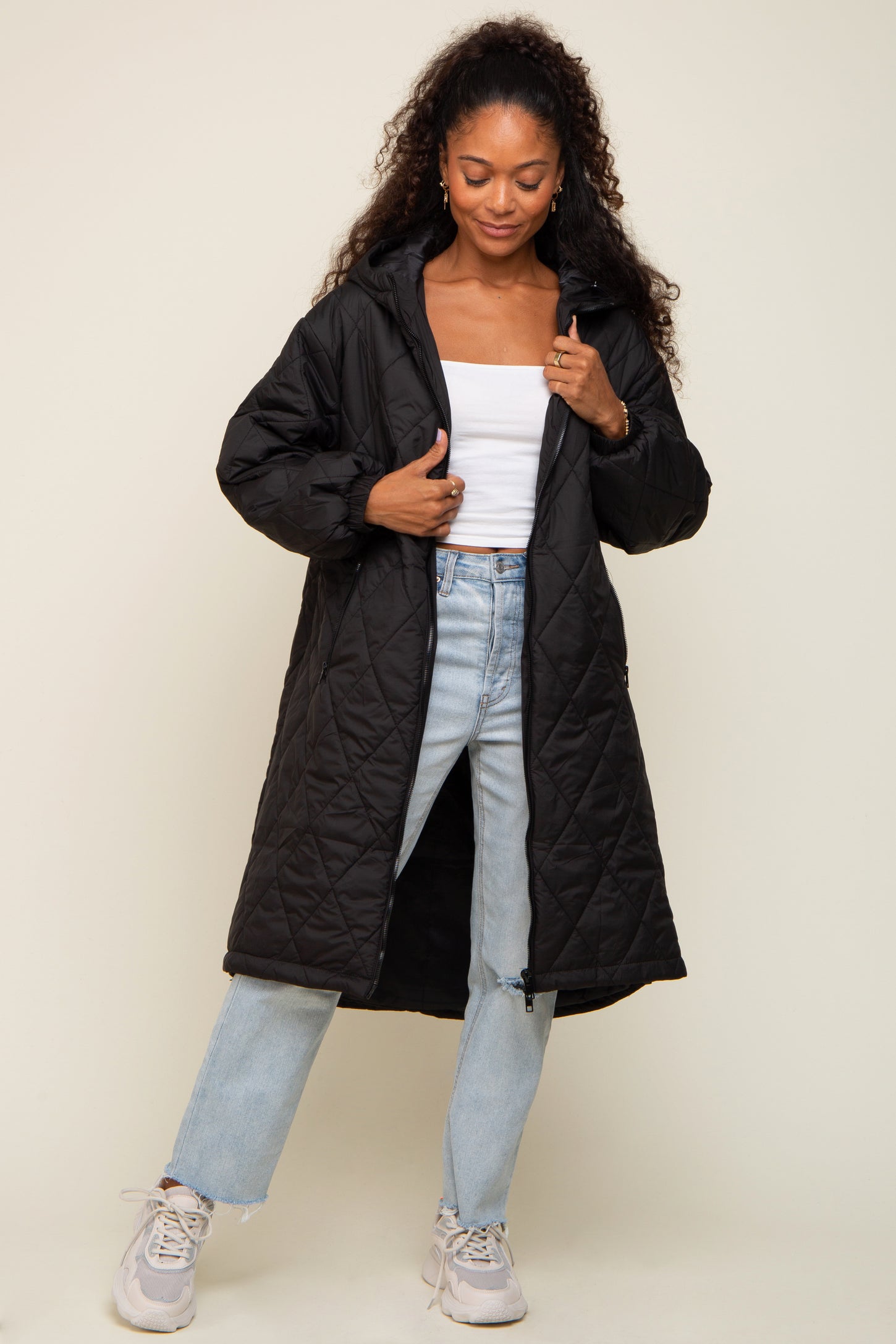 Woman wearing a long black quilted puffer coat with a hood over a white top and light wash jeans