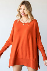 woman wearing a loose-fitting orange oversized sweater with side slits and a round neckline