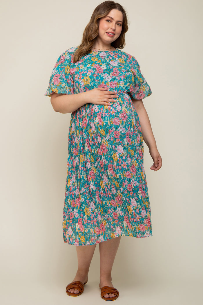 woman wearing a floral maternity plus dress in teal with short puff sleeves and holding her baby bump