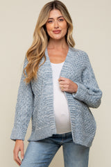 woman wearing a light blue maternity cardigan and a white top, showing her baby bump, paired with blue jeans