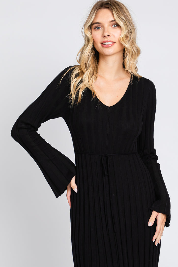 woman wearing a black ribbed long sleeve dress with a v-neck and bell sleeves, featuring a tie at the waist
