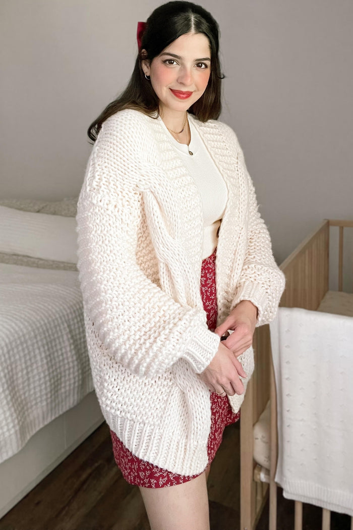 woman wearing a fluffy light pink oversized cardigan with a white top and floral red skirt