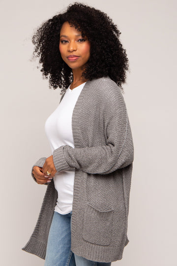 woman wearing a gray knitted cardigan over a white top and blue jeans, with curly hair styled down