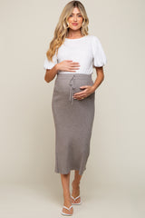 woman wearing a white puff sleeve top and a gray ribbed maternity skirt, holding her baby bump