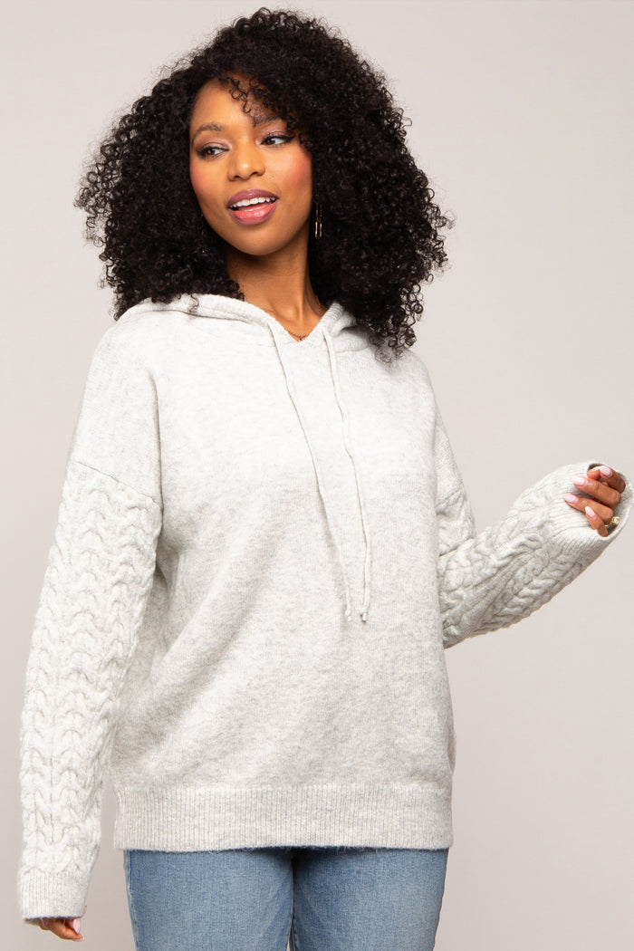 woman wearing a light gray oversized hoodie with cable knit sleeves and a drawstring hood