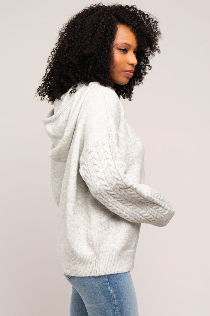 woman wearing a light gray pullover hoodie with cable-knit sleeves and a relaxed fit, paired with blue jeans