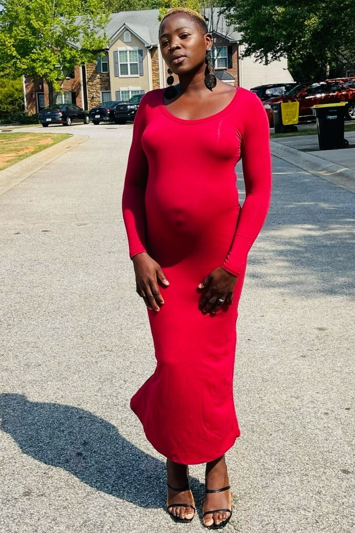 woman wearing a red long sleeve maternity dress, showing off her baby bump while standing on a street