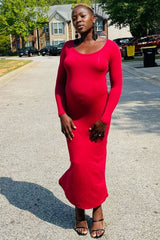 woman wearing a red long sleeve maternity dress, showing off her baby bump while standing on a street