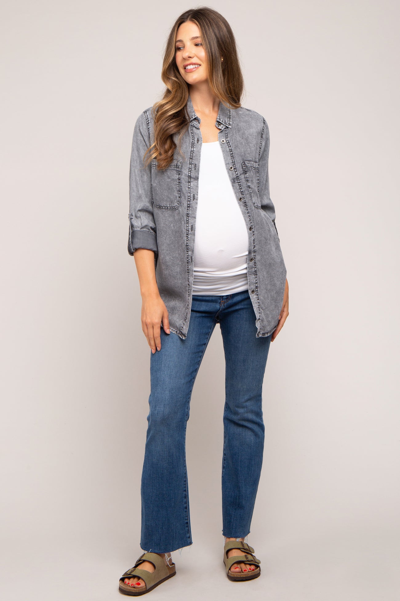 woman wearing a gray maternity button-up shirt over a white top and blue jeans, showing her baby bump