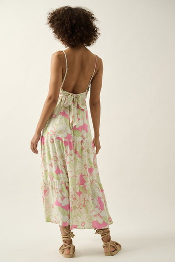 woman wearing a backless floral maxi dress in pink and green with a tie detail at the back
