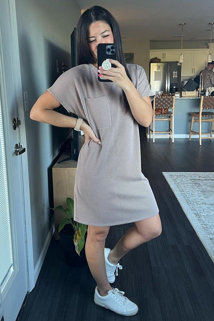 woman wearing a striped short sleeve dress with a pocket and white sneakers, posing in a bright indoor space