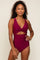woman wearing a burgundy one-piece swimsuit with a twisted front and cut-out detail, posing confidently