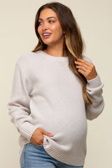 woman wearing a light beige maternity sweater with a textured pattern and a visible baby bump