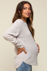 woman wearing a light gray maternity sweater, showcasing her baby bump, paired with blue jeans