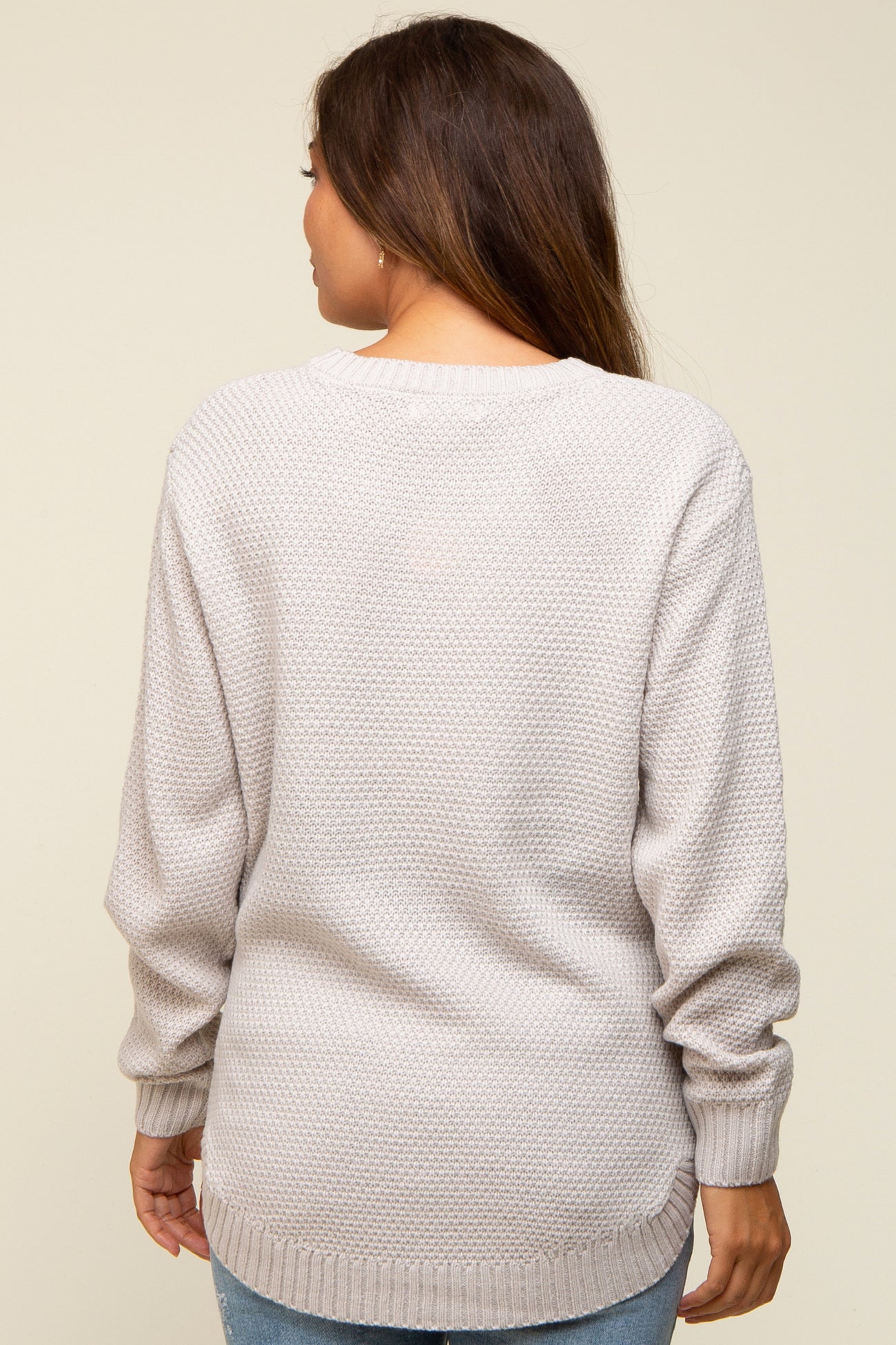 woman wearing a light gray long sleeve maternity sweater with a textured knit pattern, view from the back